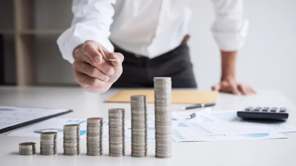 Seorang pebisnis menumpuk koin di atas meja dengan dokumen keuangan